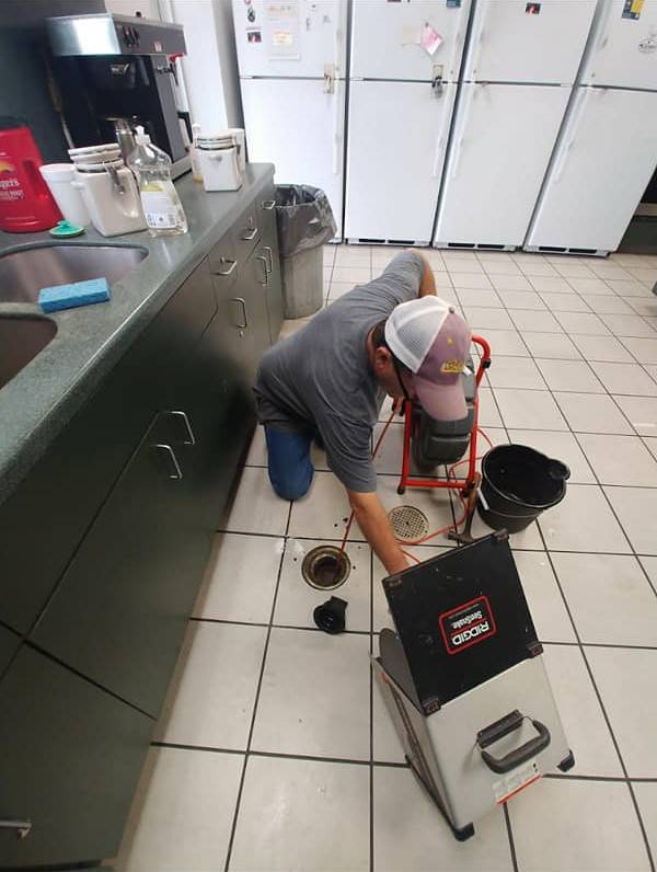 DrainCo technician clearing a floor drain in a commercial kitchen