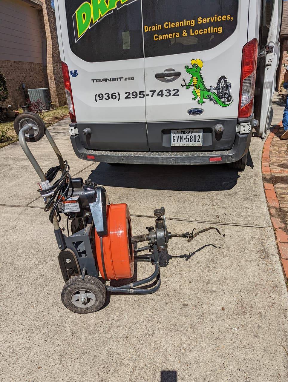 DrainCo service van with phone number and a drain machine on the driveway